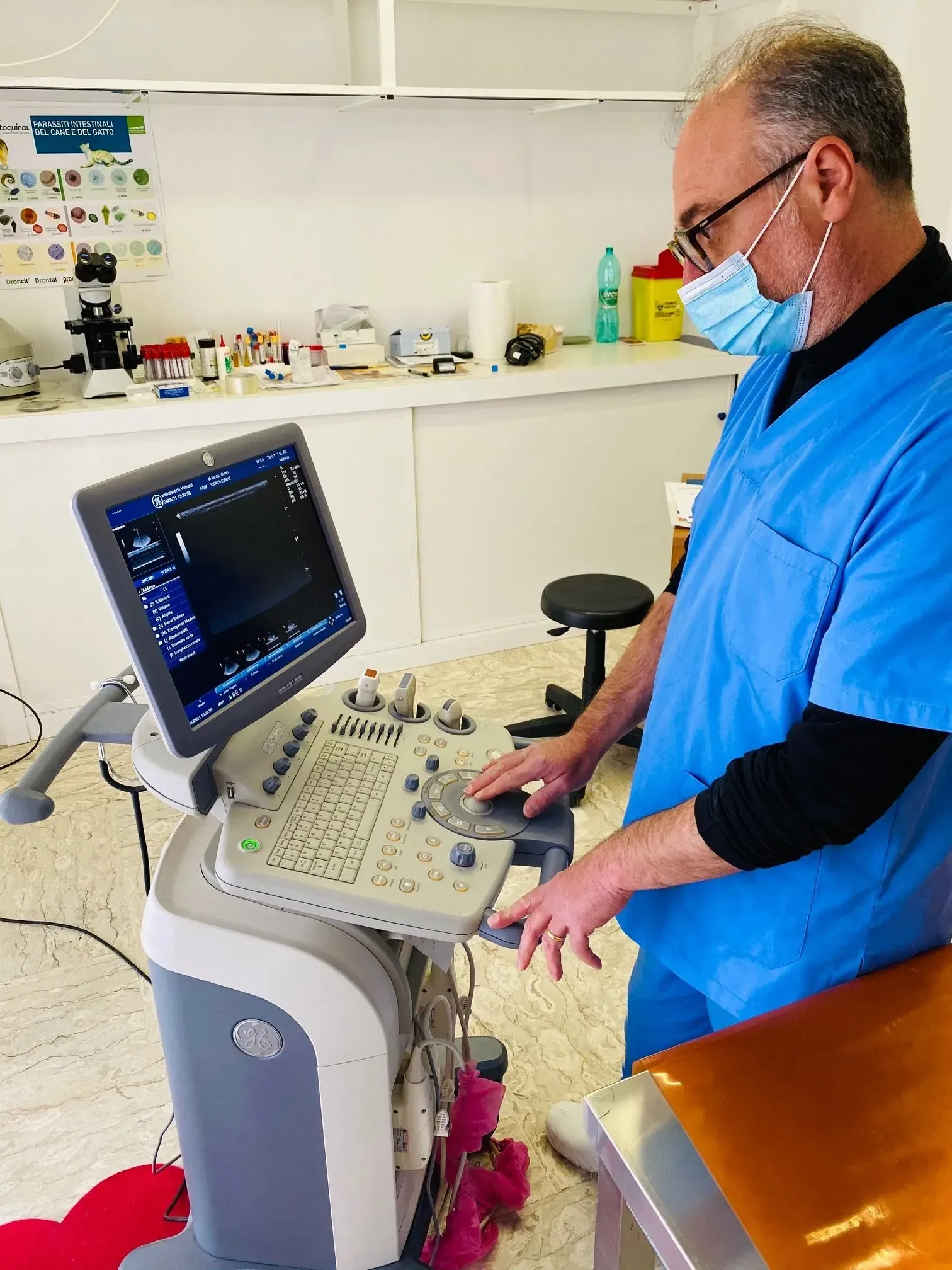 Un operatore sanitario in camice blu e mascherina utilizza un apparecchio per ecografie in un laboratorio clinico.