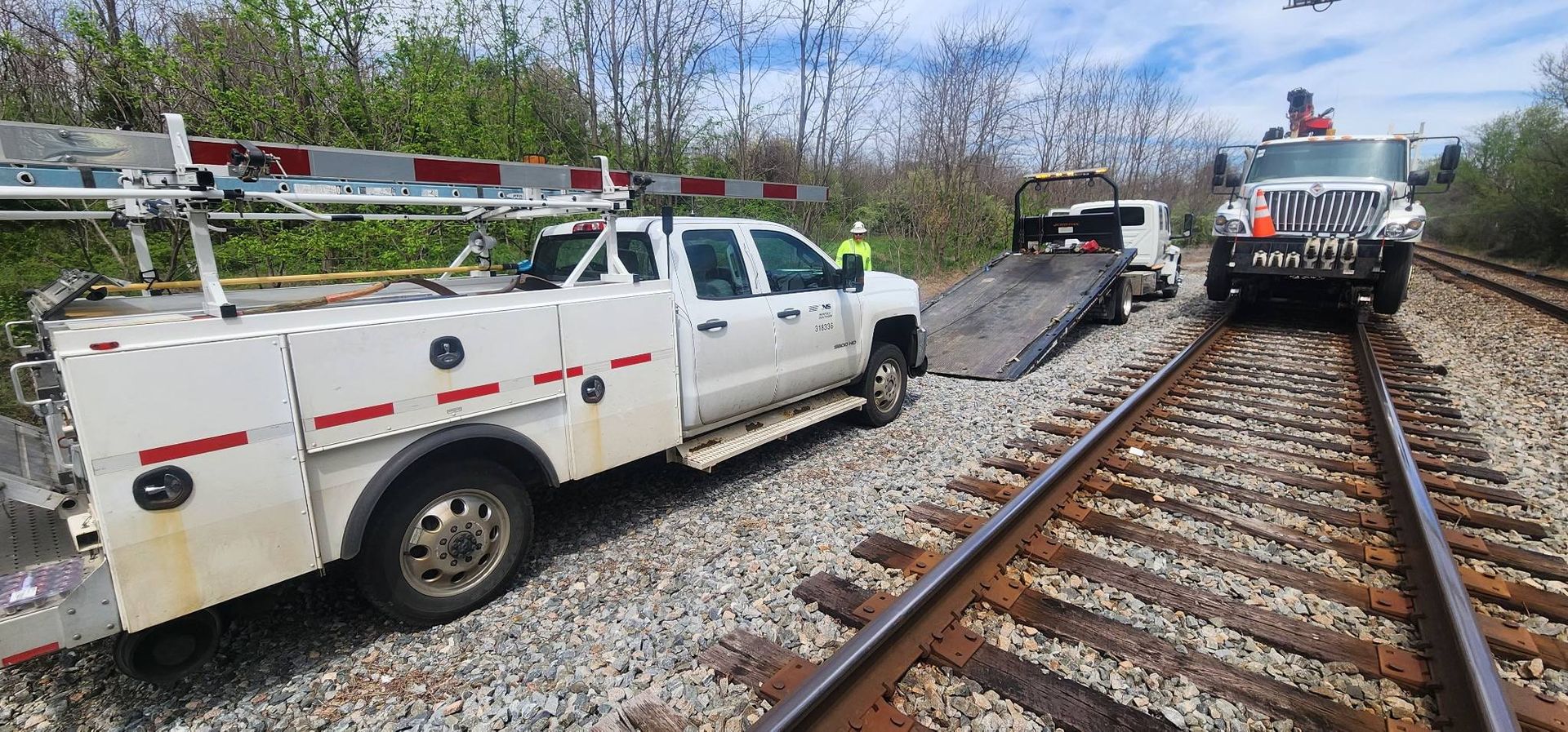 Three service trucks on railroad tracks, near a crossing barrier.