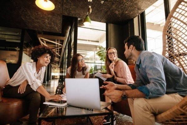A group of people are sitting around a table with a laptop.