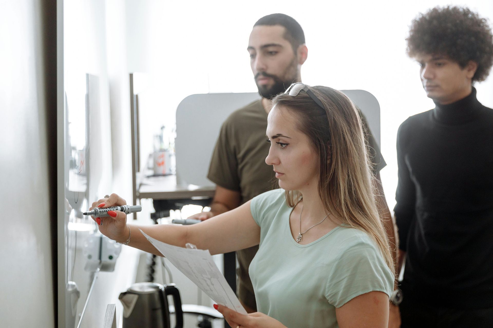 A woman is writing on a whiteboard while two men look on.