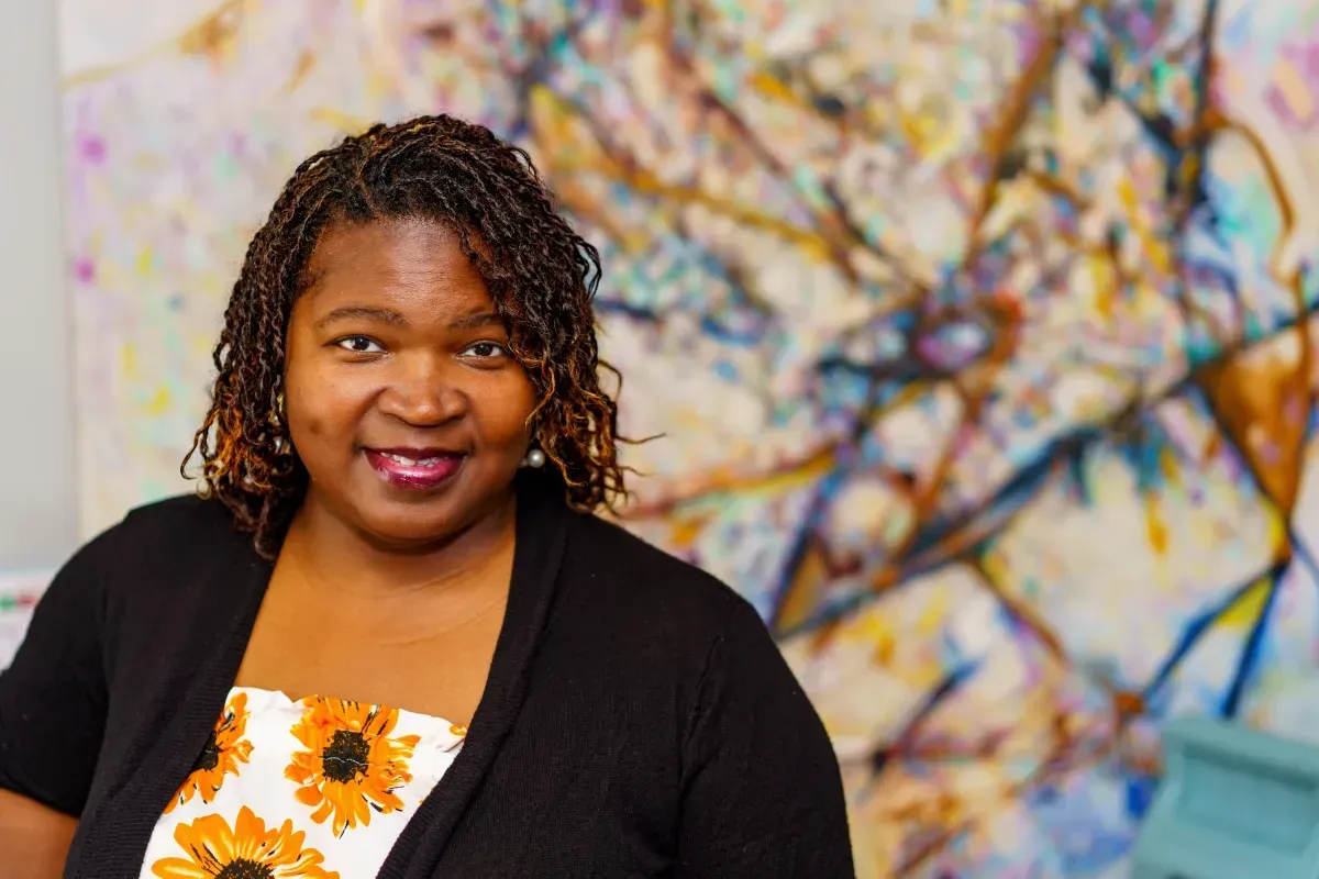 A woman is standing in front of a colorful painting.