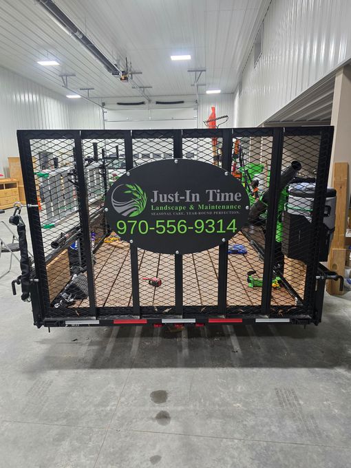 Black mesh trailer gate with green “Jim-In Time” logo and phone number in a warehouse alley