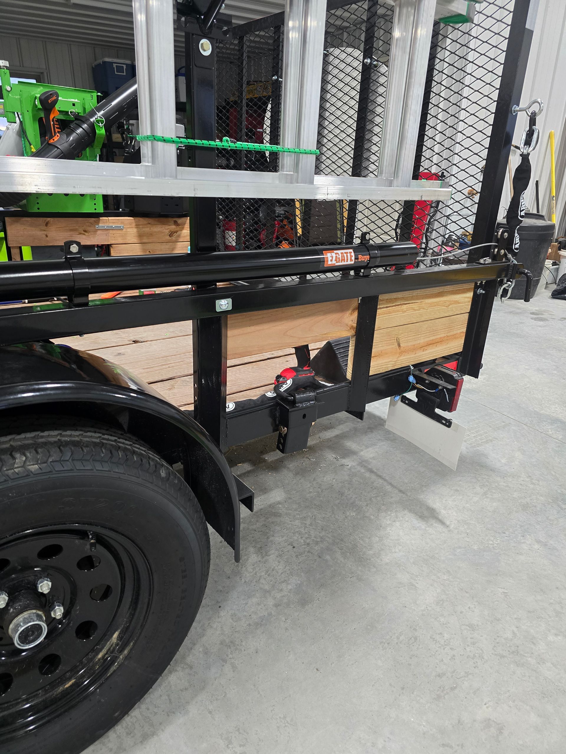 Black trailer with metal frame, wooden storage boxes, and large tire in an indoor warehouse setting