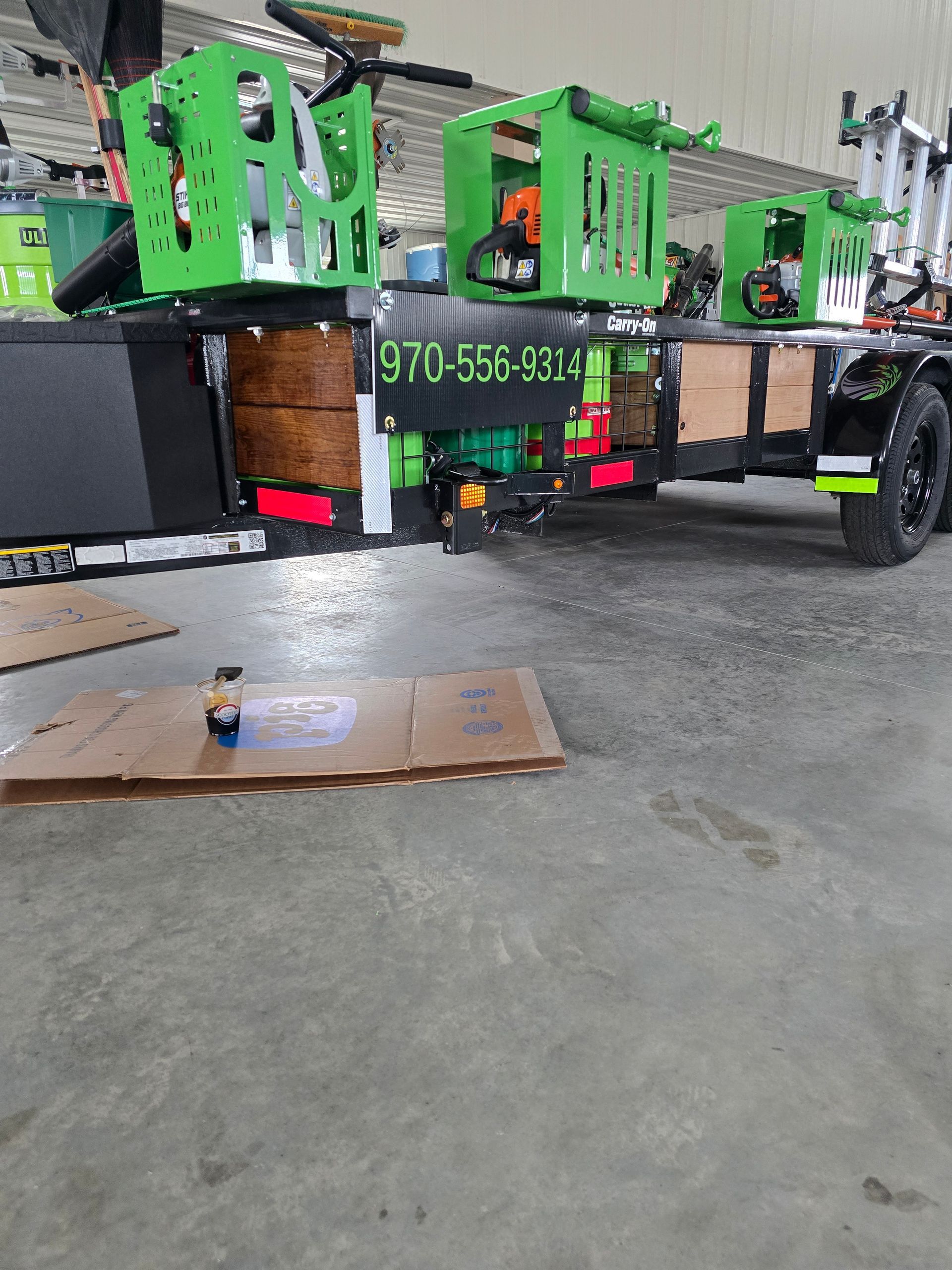 Green utility truck with trailer in a garage, with a cardboard box on the concrete floor.