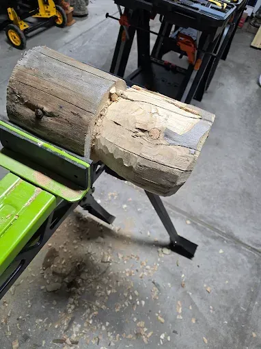Damaged split wooden log on a metal stand in a workshop, with wood chips scattered below