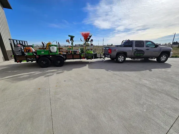Gray pickup towing a green trailer with farm equipment in a parking lot on a sunny day
