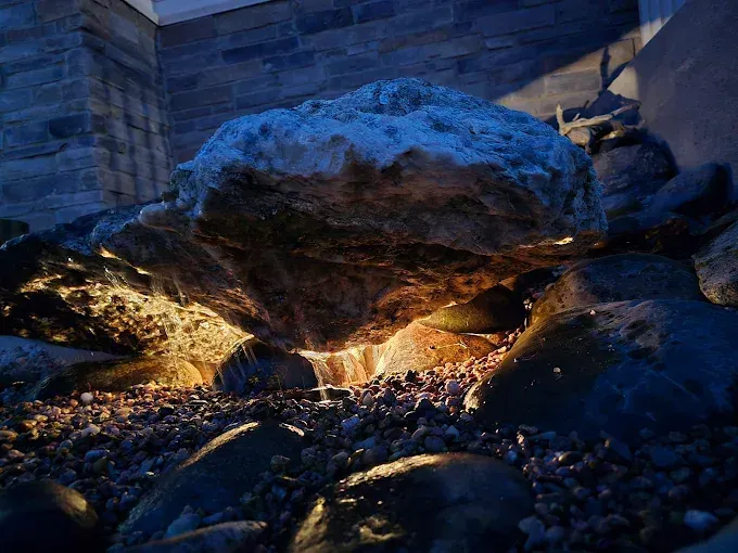 Illuminated rock formation over a shallow stream at night, with stone walls in the background