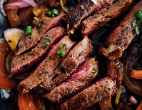 A close up of a steak with onions and tomatoes on a plate.