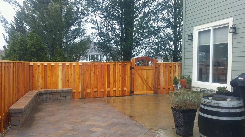 Wet patio with wooden fence, built-in bench, potted plants, and a house exterior.