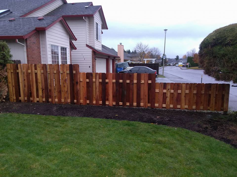 Wooden privacy fence beside a house, with a green lawn and cloudy suburban street in the background.