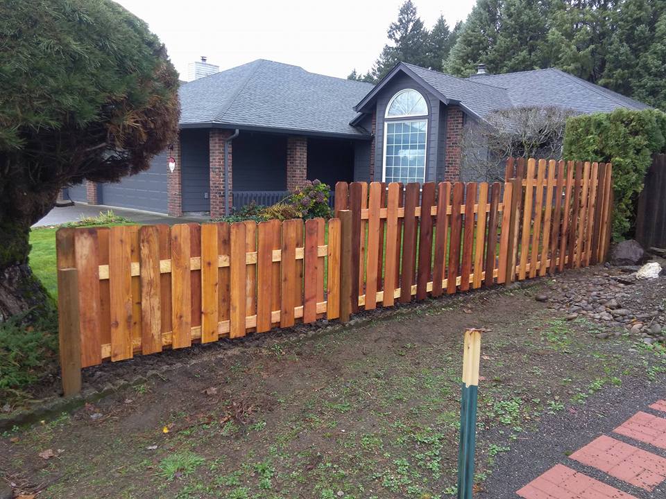 Wooden privacy fence along a dark house yard, with a green lawn and brick walkway in front