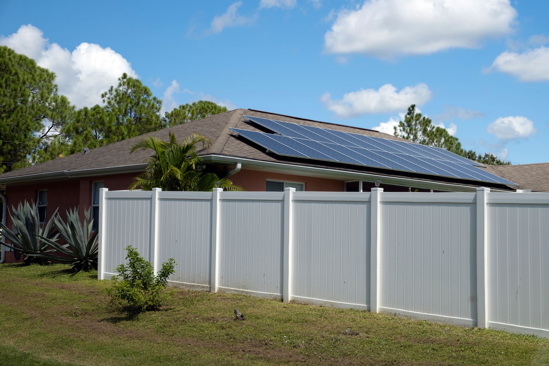 White vinyl privacy fence around a backyard beside a home with rooftop solar panels.