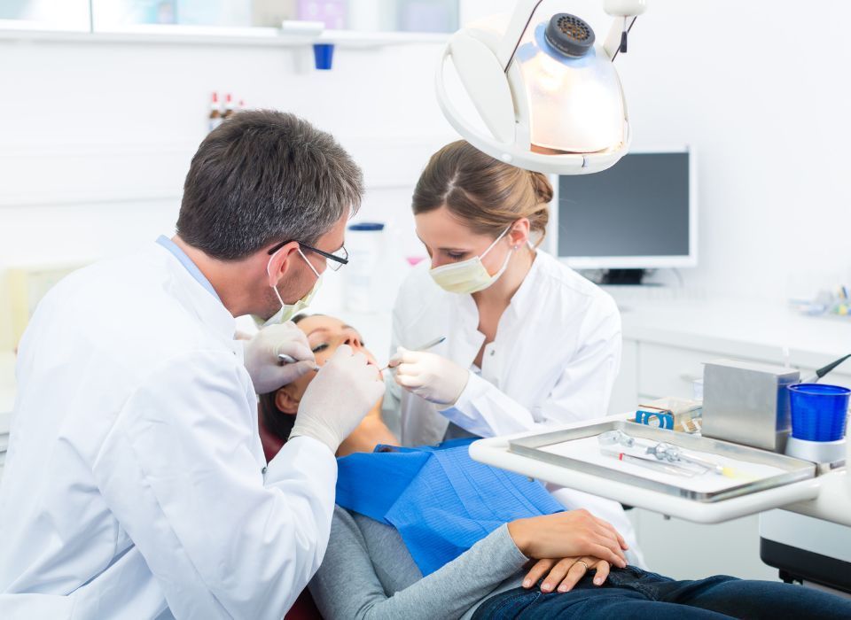 Dentist examining a patient's teeth with an assistant in a dental office.