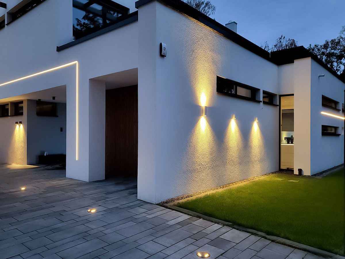 Moderne Fassadenbeleuchtung: Lineare LED-Lichtbänder, Up-and-Downlights und Bodeneinbaustrahler in der Einfahrt.