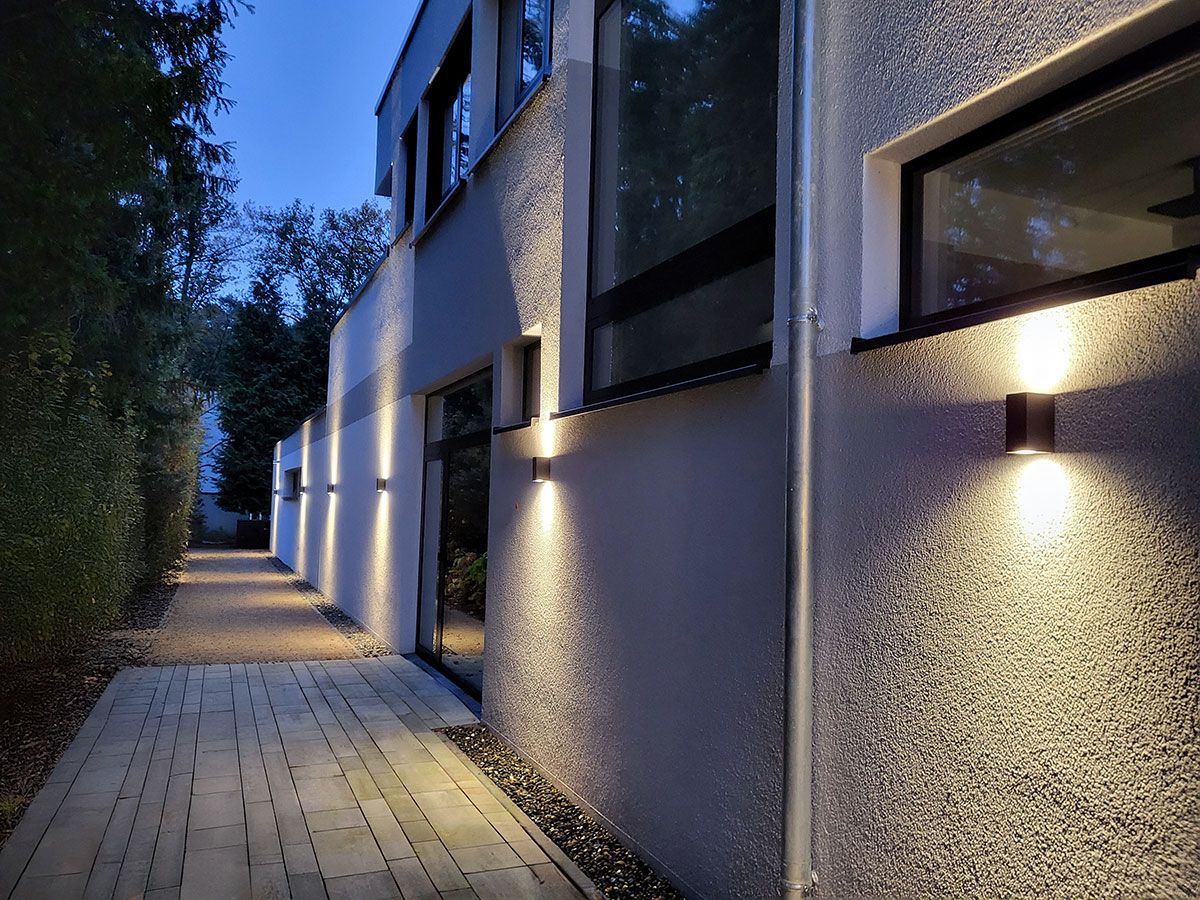 Moderne Außenbeleuchtung der Fassade mit Up-and-Down-Wandstrahlern entlang des Gehwegs.