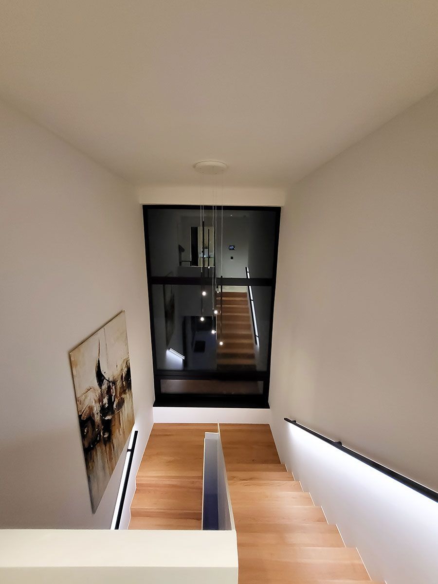 Projektbeispiel Lichtplanung: Moderne Pendelleuchte als Blickfang in einem Treppenhaus mit Holzstufen