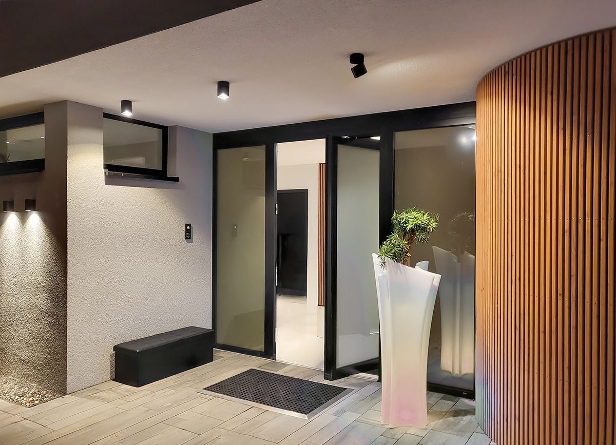 Projektbeispiel Lichtplanung: Drei moderne Aufbauspots beleuchten einen Wohnungseingang mit schwarzen Glastüren