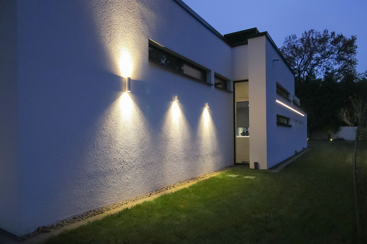 Moderne Fassadenbeleuchtung mit Up-and-Down-Wandleuchten und einem linearen LED-Lichtband.