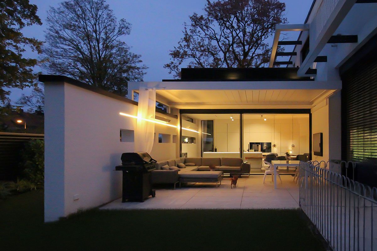 Terrassenbeleuchtung bei Dämmerung: Ein warmweißes LED-Lichtband verbindet die Außenwand mit dem hellen Innenbereich.