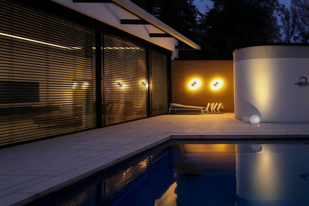 Lichtplanung im Außenbereich: Geometrische Wandleuchten, Kugelleuchten am Boden und Lichtreflexionen im Pool.