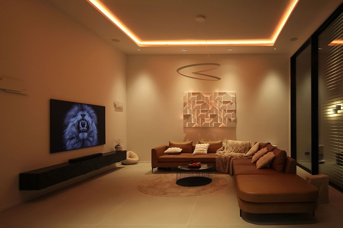 Wohnraumbeleuchtung: Warmweiße LED-Voutenbeleuchtung an der Decke und hinterleuchtetes Wandrelief über Sofa.