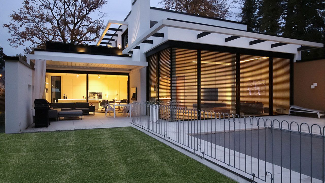 Architekturbeleuchtung bei Dämmerung: Warmes Innenlicht strahlt durch große Glasfronten sanft auf Terrasse und Garten.