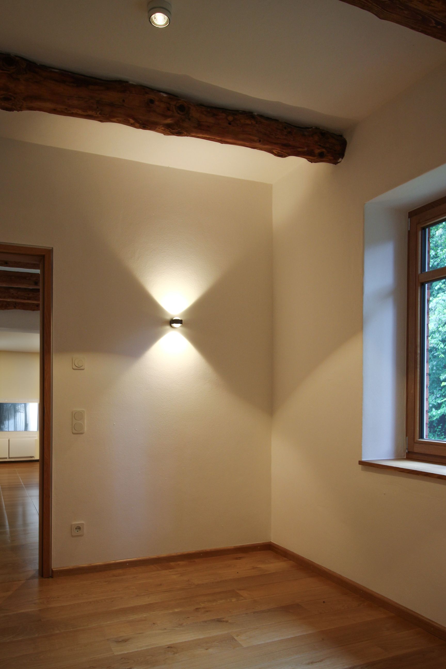 Altbau-Akzentbeleuchtung: Up-and-Down-Linsenleuchte wirft sanduhrförmiges Licht an die Wand, ergänzt durch Strahler.