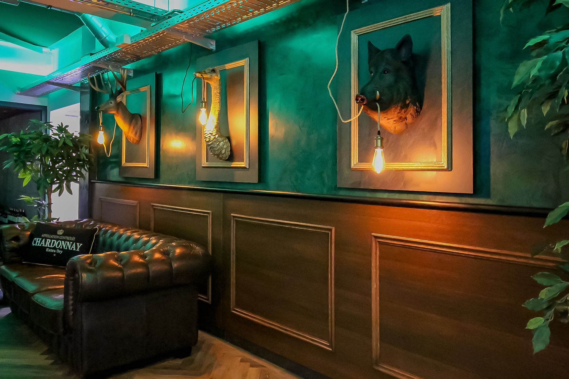 Extravagante Bar-Beleuchtung: Grünes LED-Deckenlicht und hängende Vintage-Glühbirnen an Tierkopf-Skulpturen.