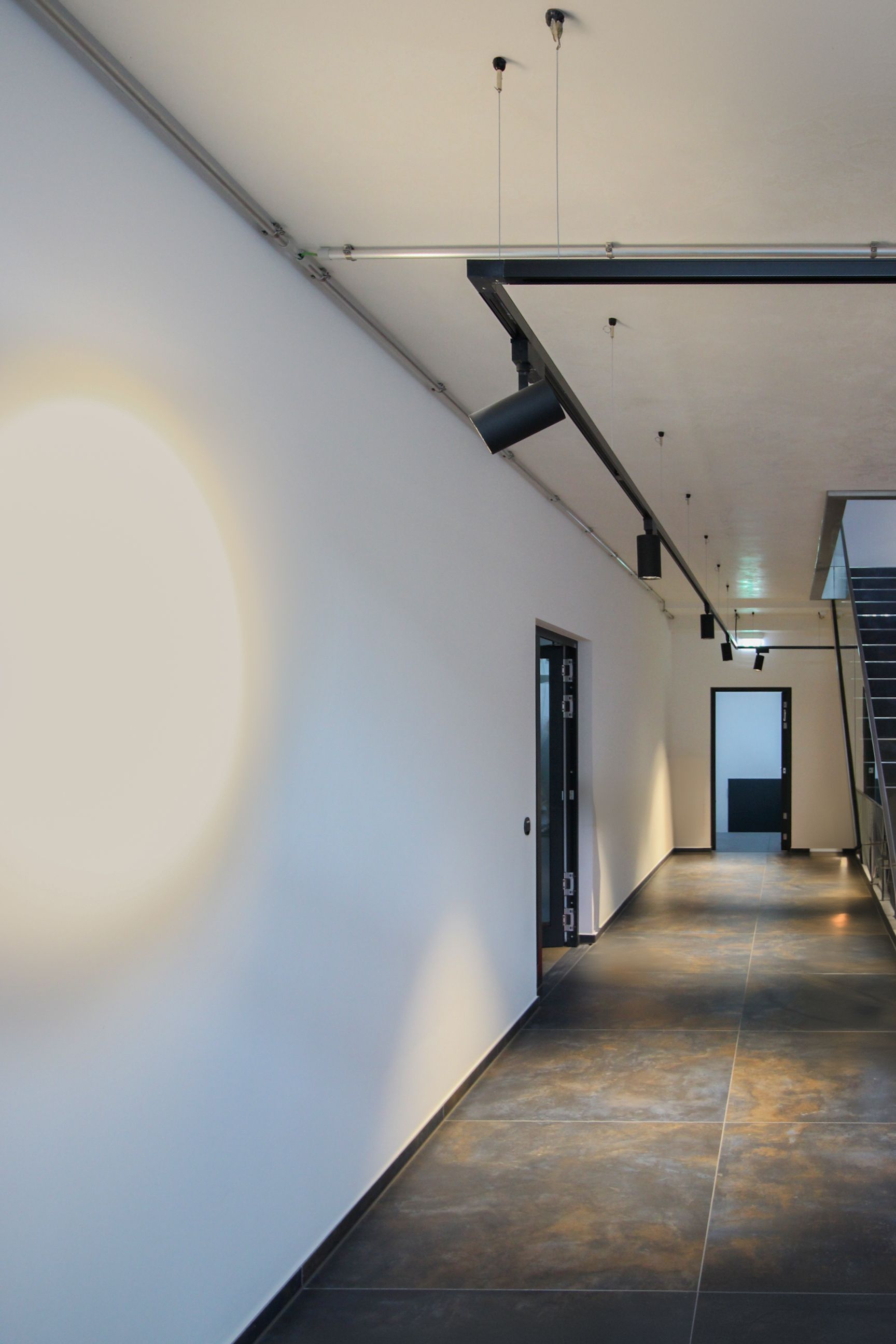 Fokussierte Flurbeleuchtung mit einem Decken-Stromschienensystem und runder Wand-Lichtkorona.