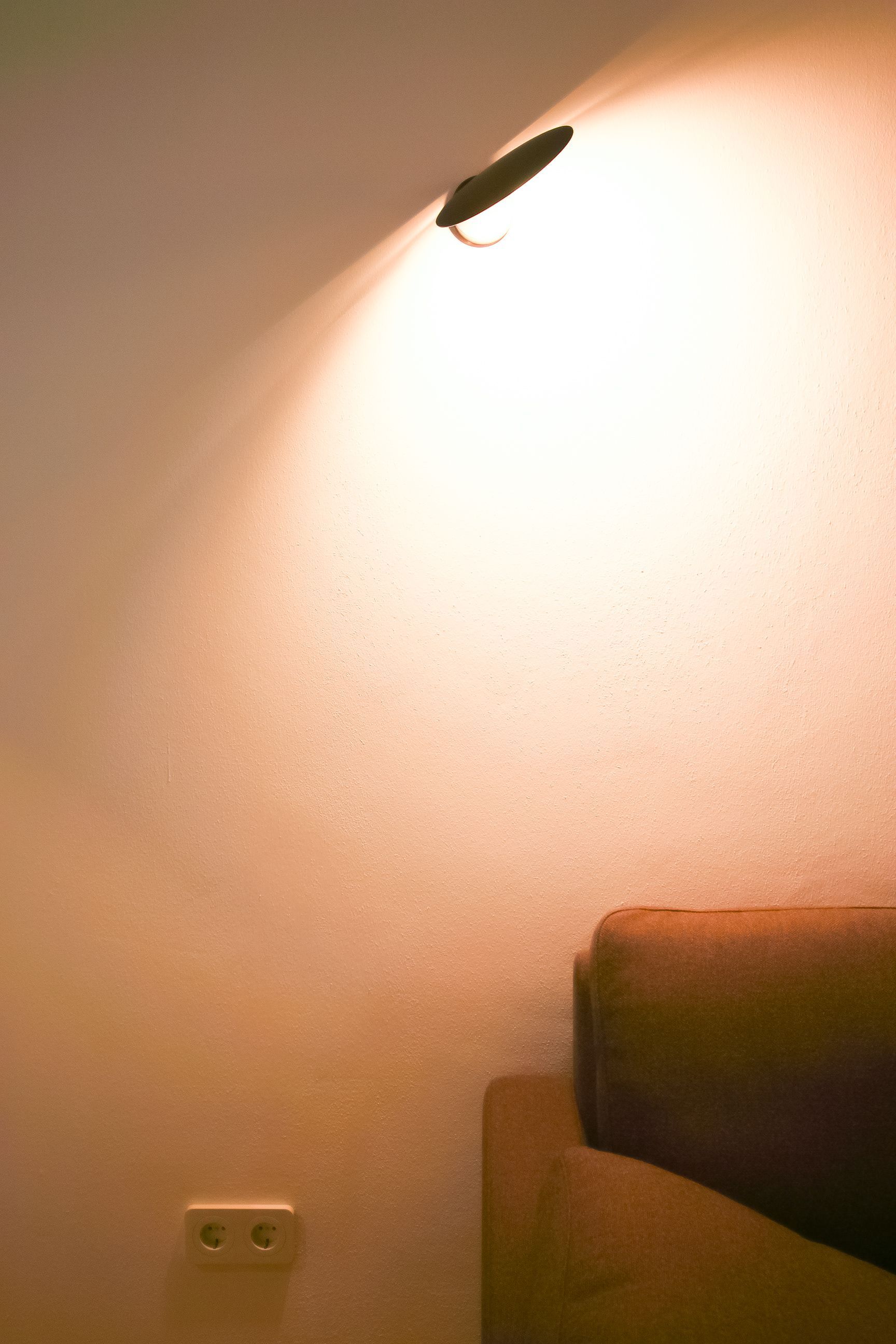 Gemütliche Wandbeleuchtung: Die flexible Leuchte Puzzle Round von Lodes wirft einen warmen Lichtkegel über das Sofa.