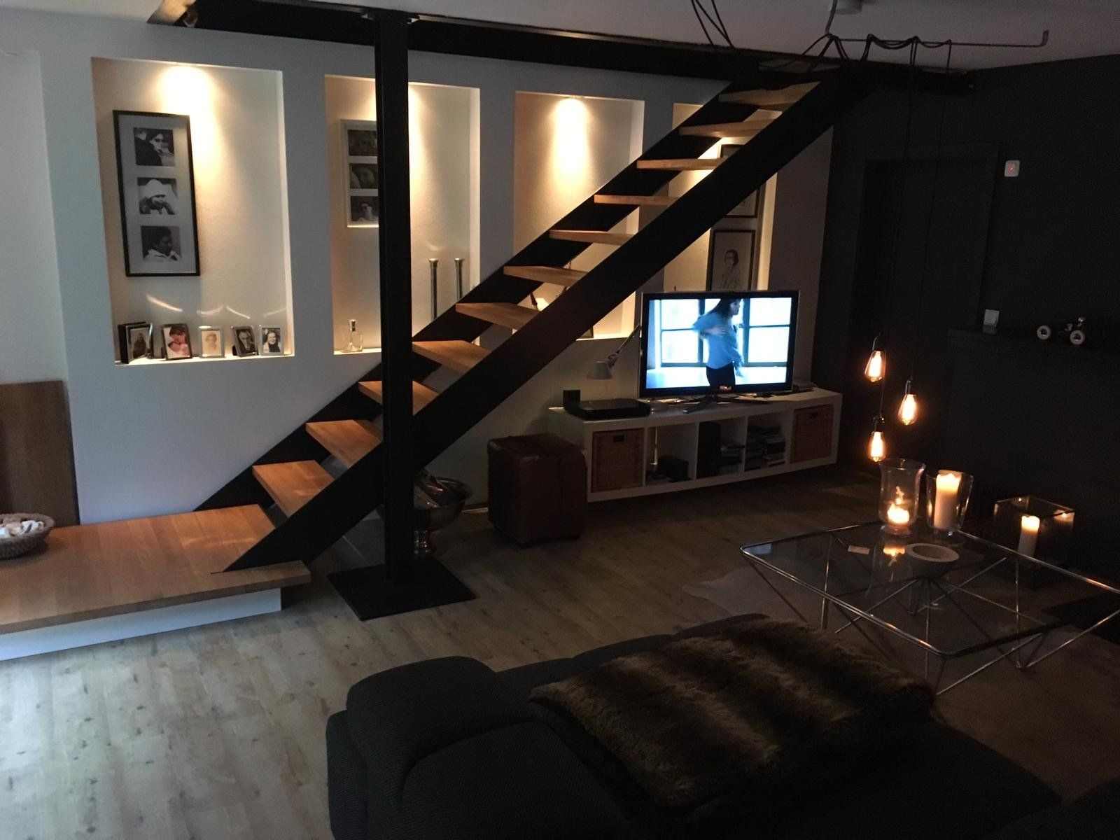 Modernes Wohnzimmer mit offener Treppe, TV-Bank, Nischenbeleuchtung und warmen Pendelleuchten am Abend.