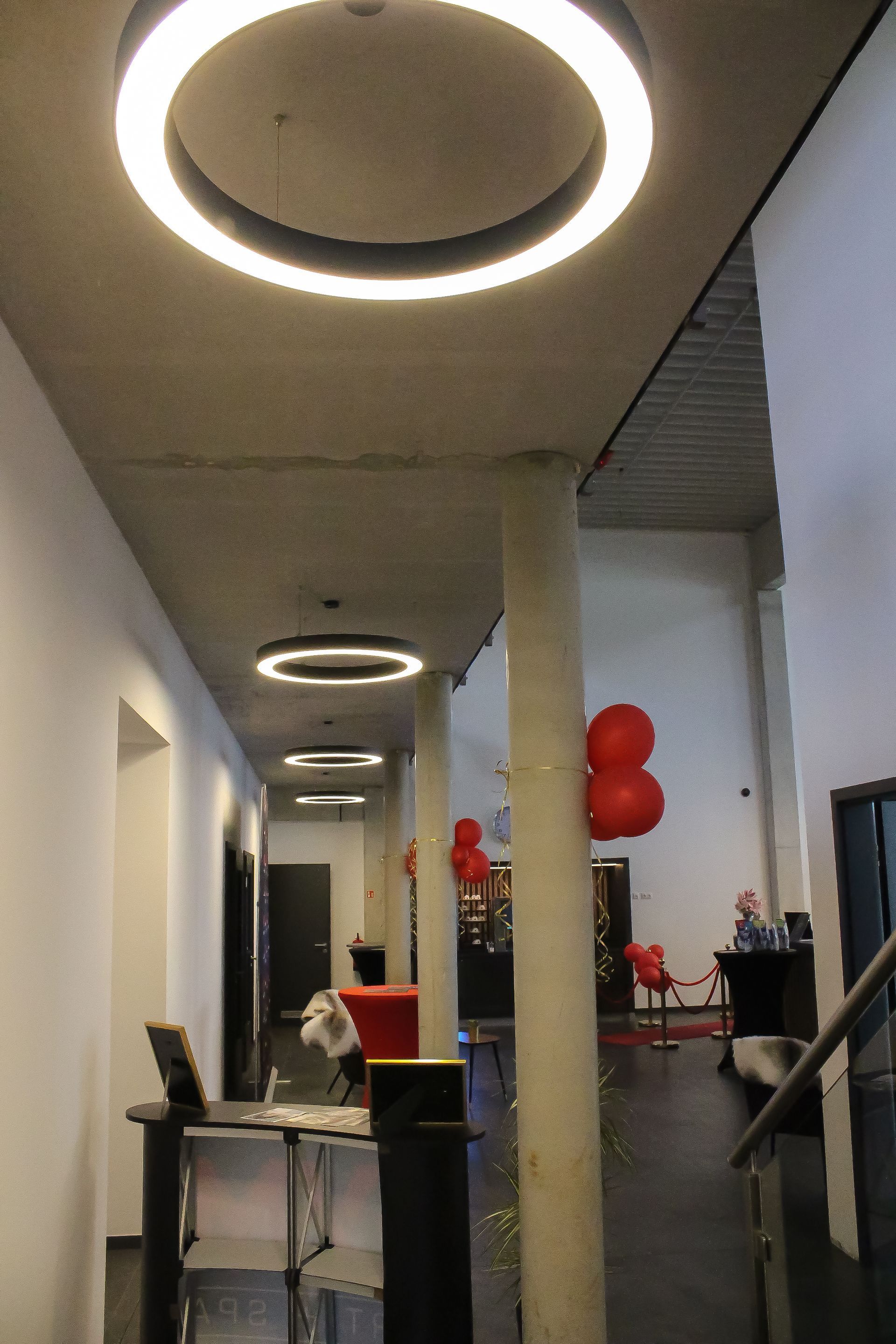 Moderne Flurbeleuchtung: Hintereinander hängende Lightnet LED-Ringleuchten leuchten den Gang an Betonstützen hell aus.