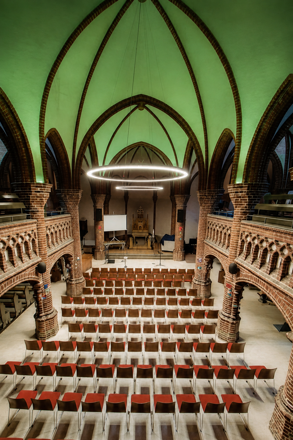 Innenraum der Gospelkirche Hannover mit zwei großen Ringleuchten, die das neugotische Backsteingewölbe indirekt beleuchten
