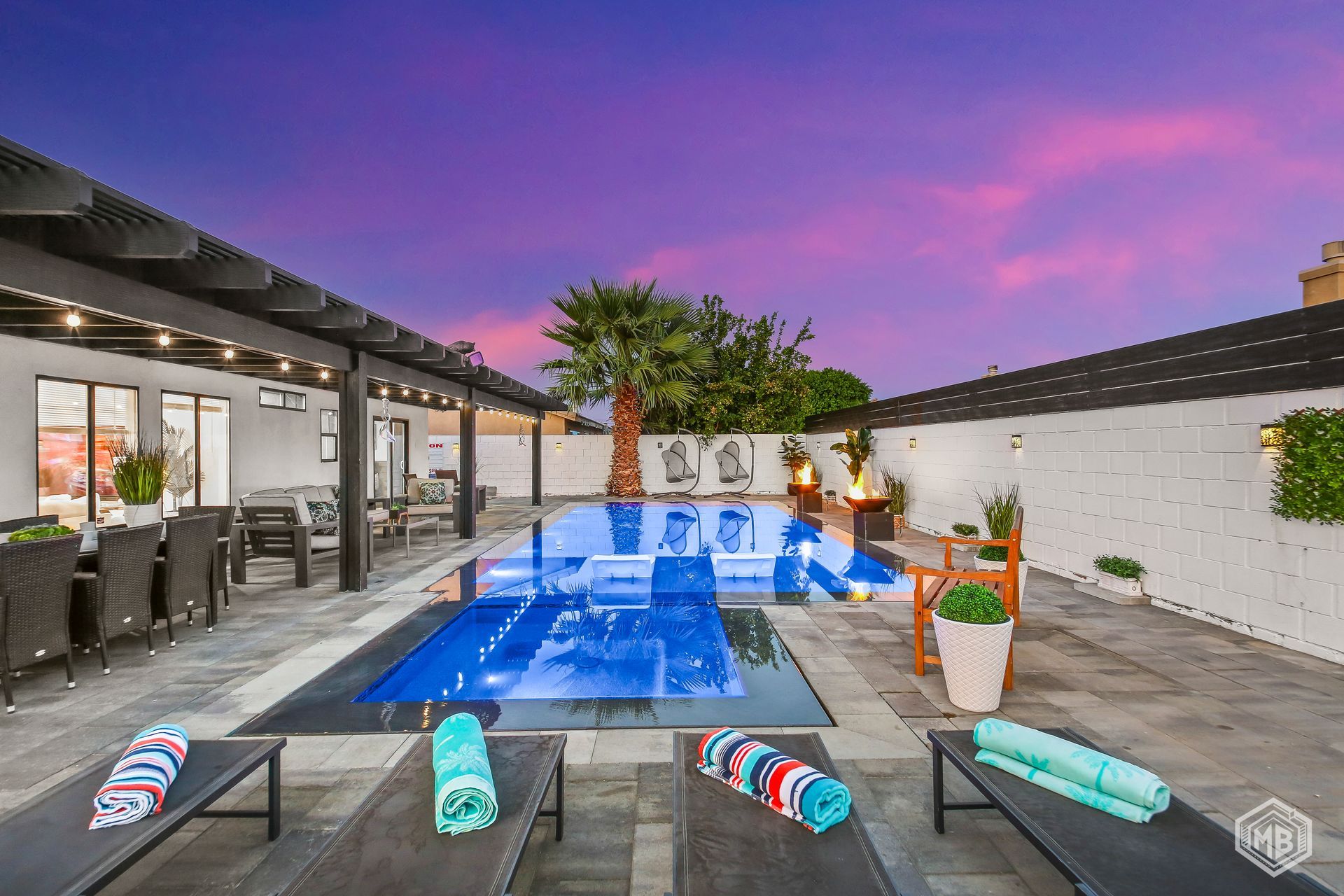 A modern backyard pool area with lounge chairs, a patio, and a vibrant purple sunset in the background.