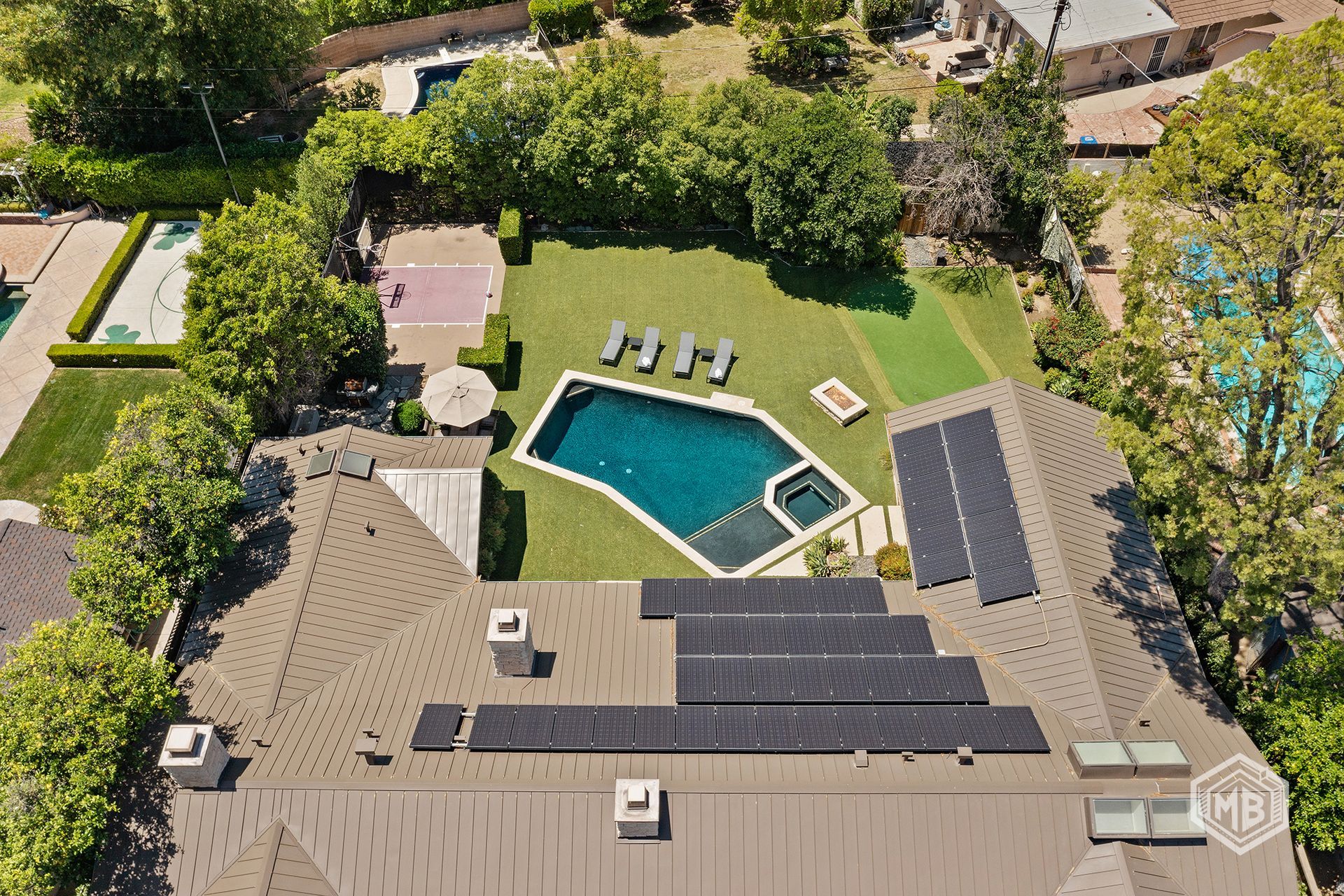 An aerial view of a house with solar panels on the roof, featuring a backyard with a swimming pool and green lawn.