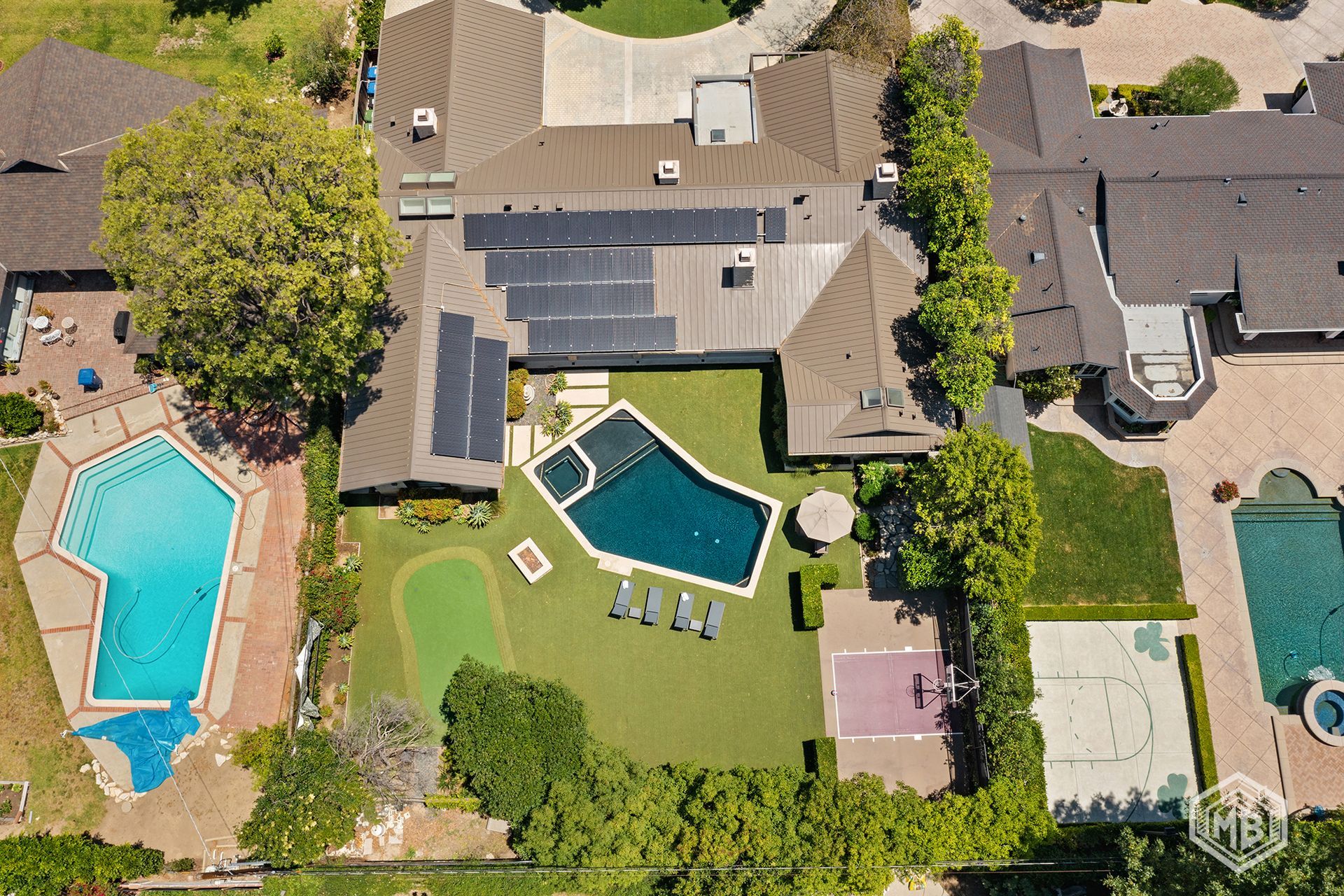 Aerial view of a residential property with three swimming pools, a putting green, and solar panels on the roof.