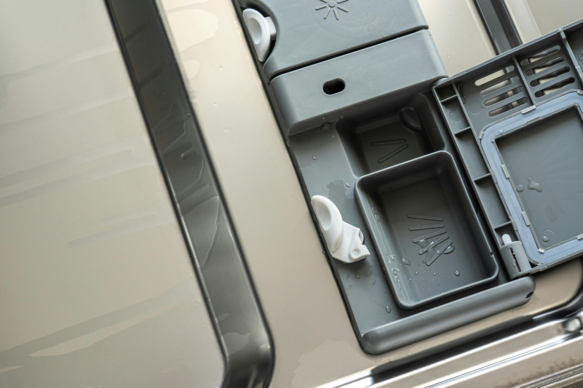 The open soap dispenser and rinse aid compartment on the inside of a dishwasher door.