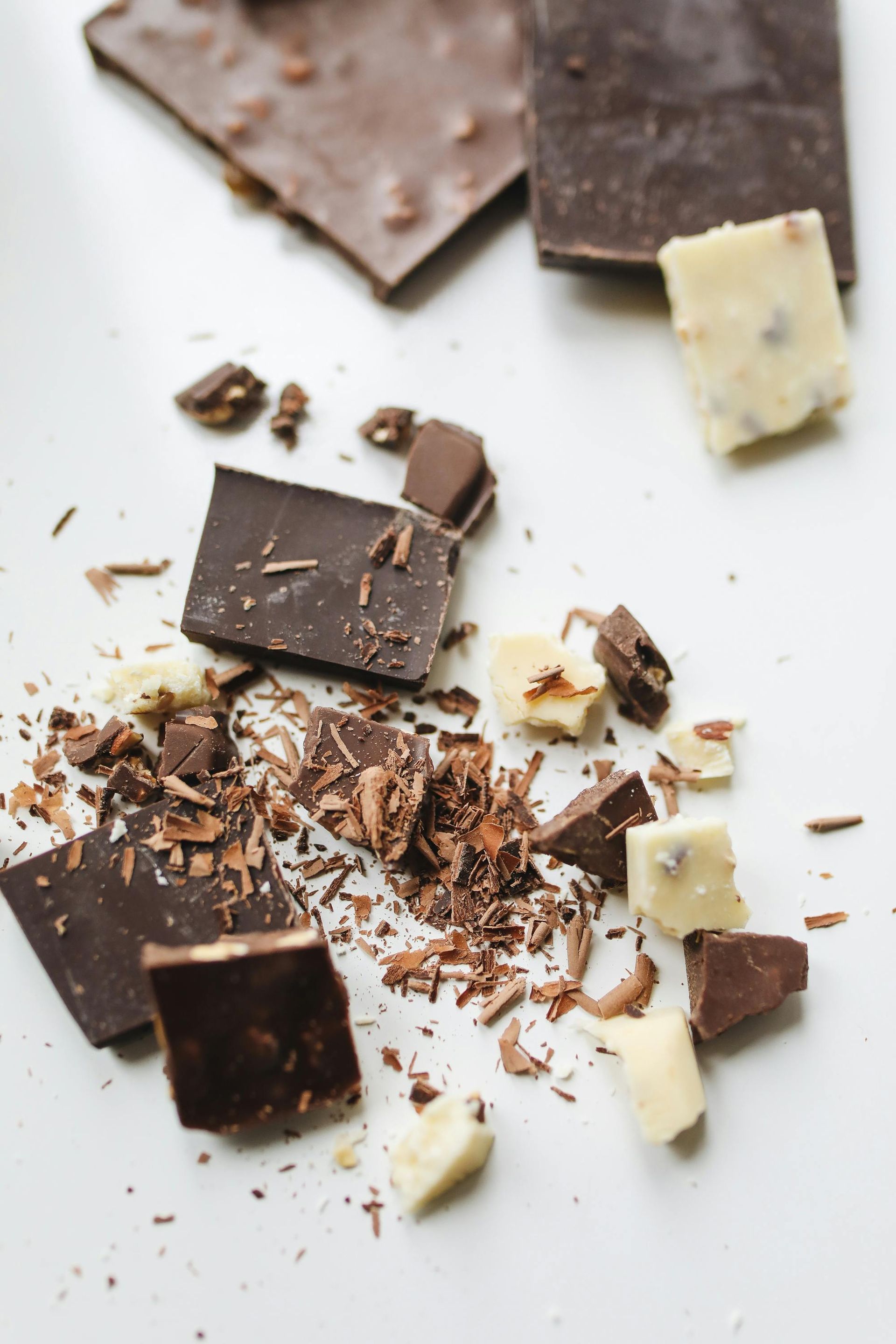 Broken pieces and shavings of dark and white chocolate scattered on a white surface.