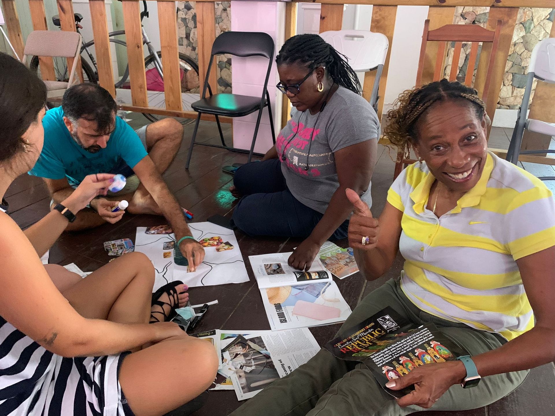 People seated on the floor, working on projects. One woman smiles and gives a thumbs up.