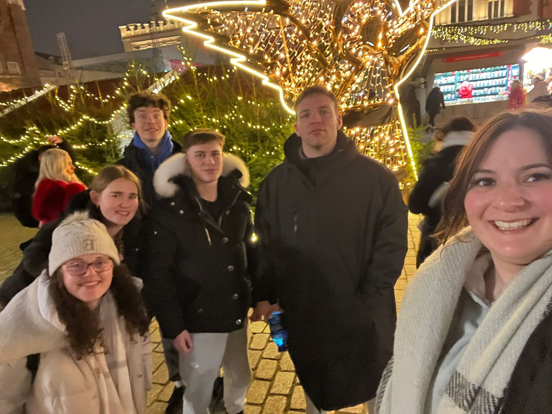Group of people taking a selfie at a Christmas market. Bright lights, smiling faces.