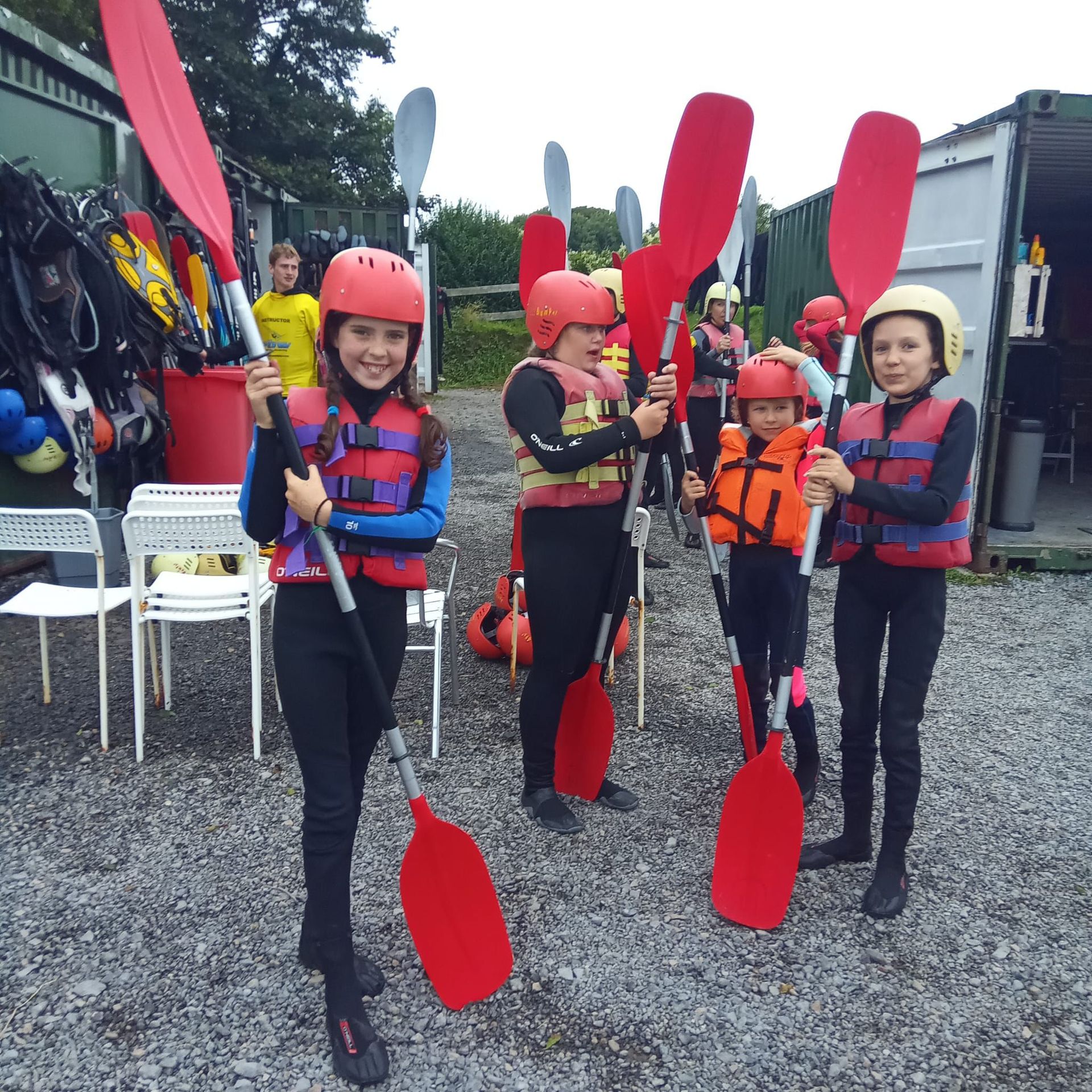 Five people in safety gear holding paddles in front of a storage container.