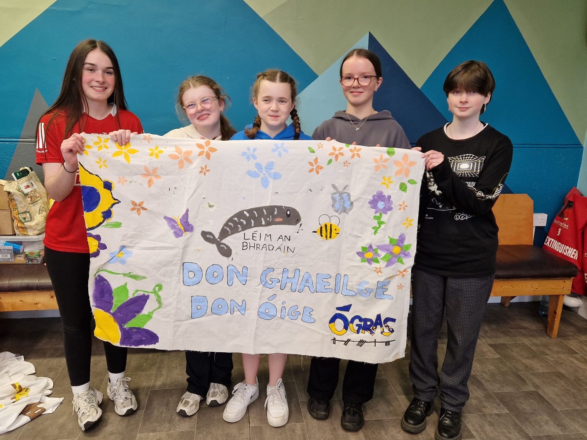 Five young people holding a painted banner with a whale and flowers.