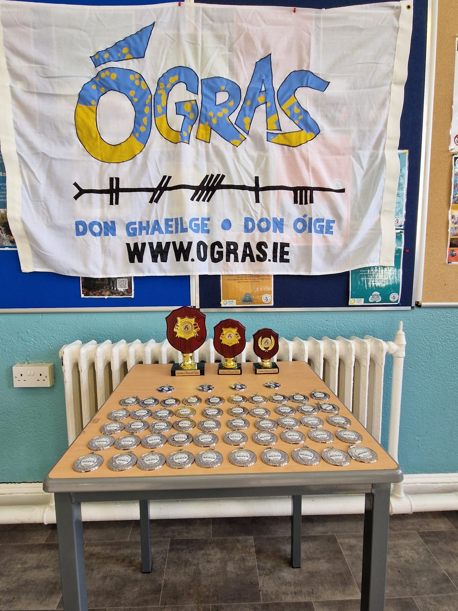 Table with trophies and medals in front of an Ógras banner.