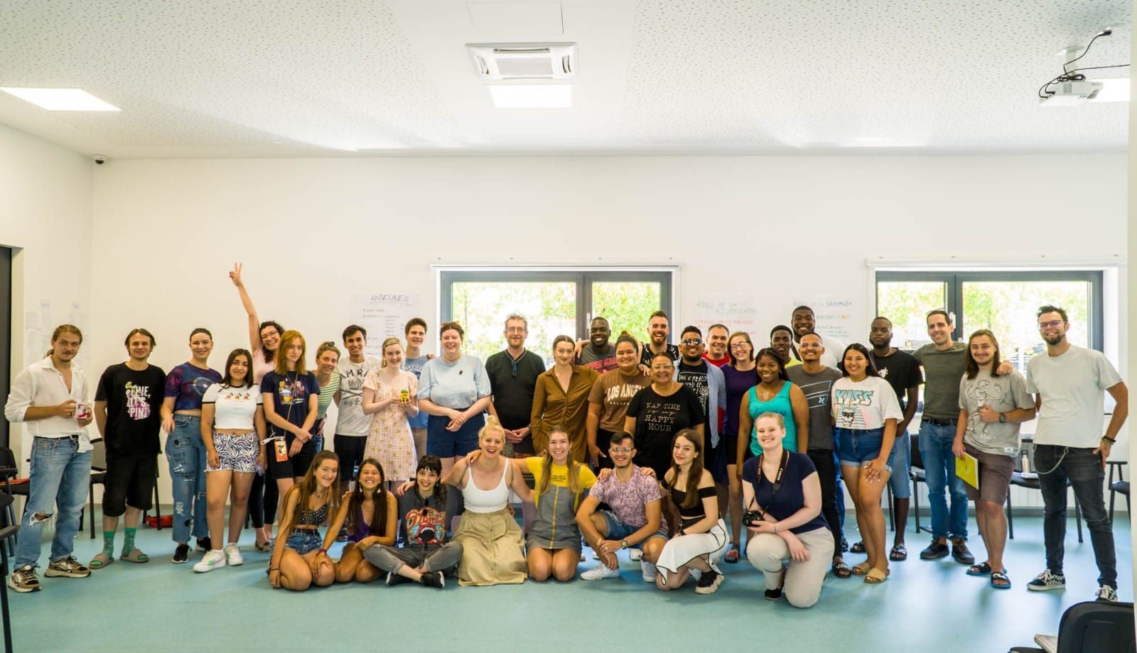 Group of people gathered in a bright room. Some are standing, others sitting. Smiling faces, some with arms raised.