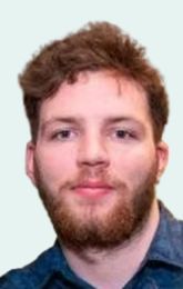 Man with reddish-brown beard and hair, wearing a dark blue collared shirt, looking forward with a neutral expression.