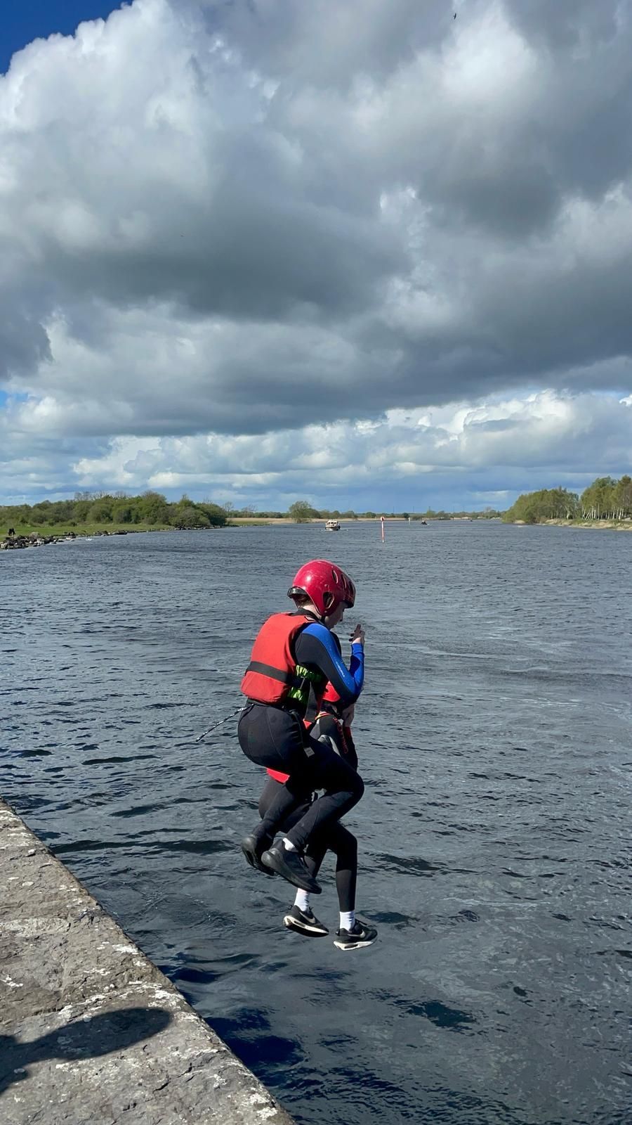 Person jumps into water from a concrete structure, wearing a helmet and life vest.