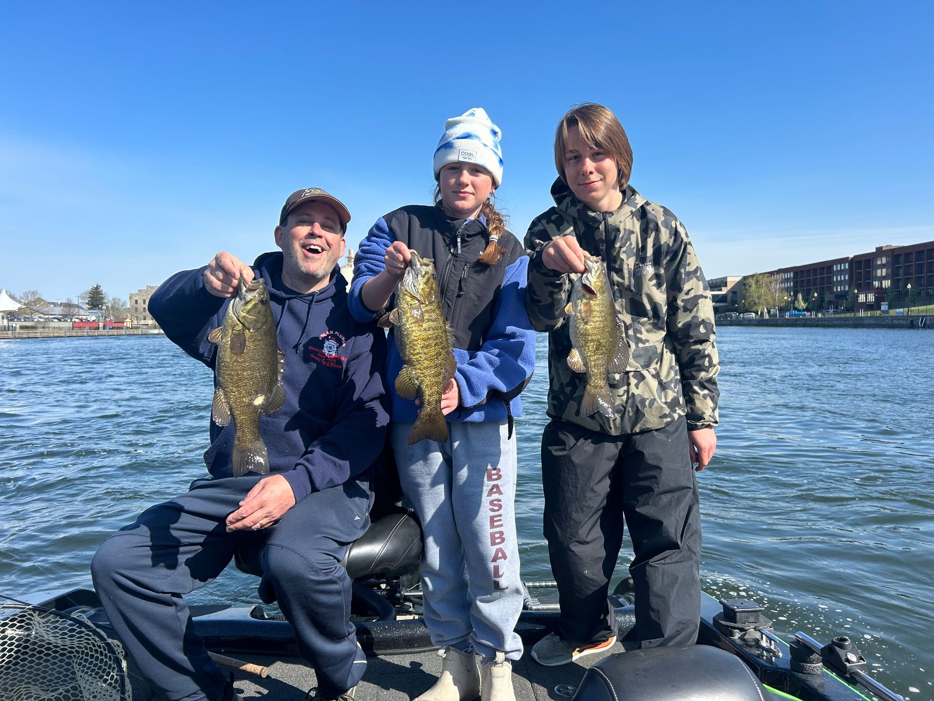 Three people are standing on a boat holding fish.