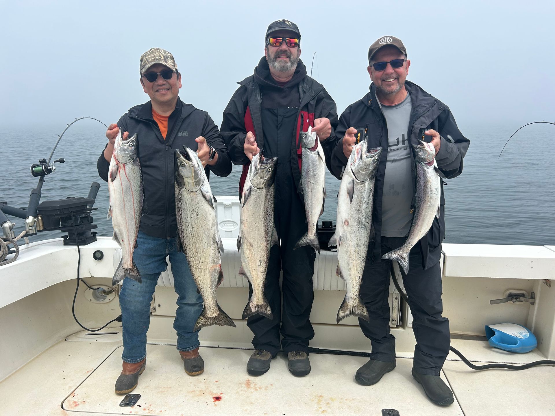 Three men are standing on a boat holding fish.