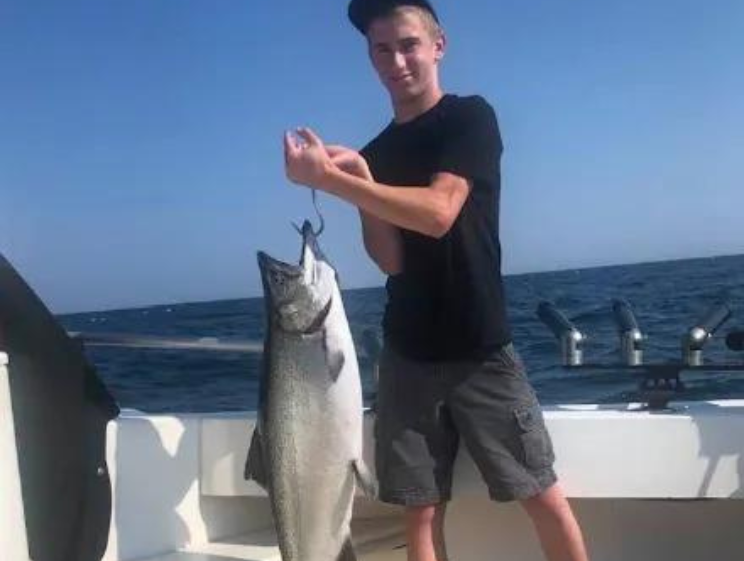 A young man is holding a large fish on a boat.