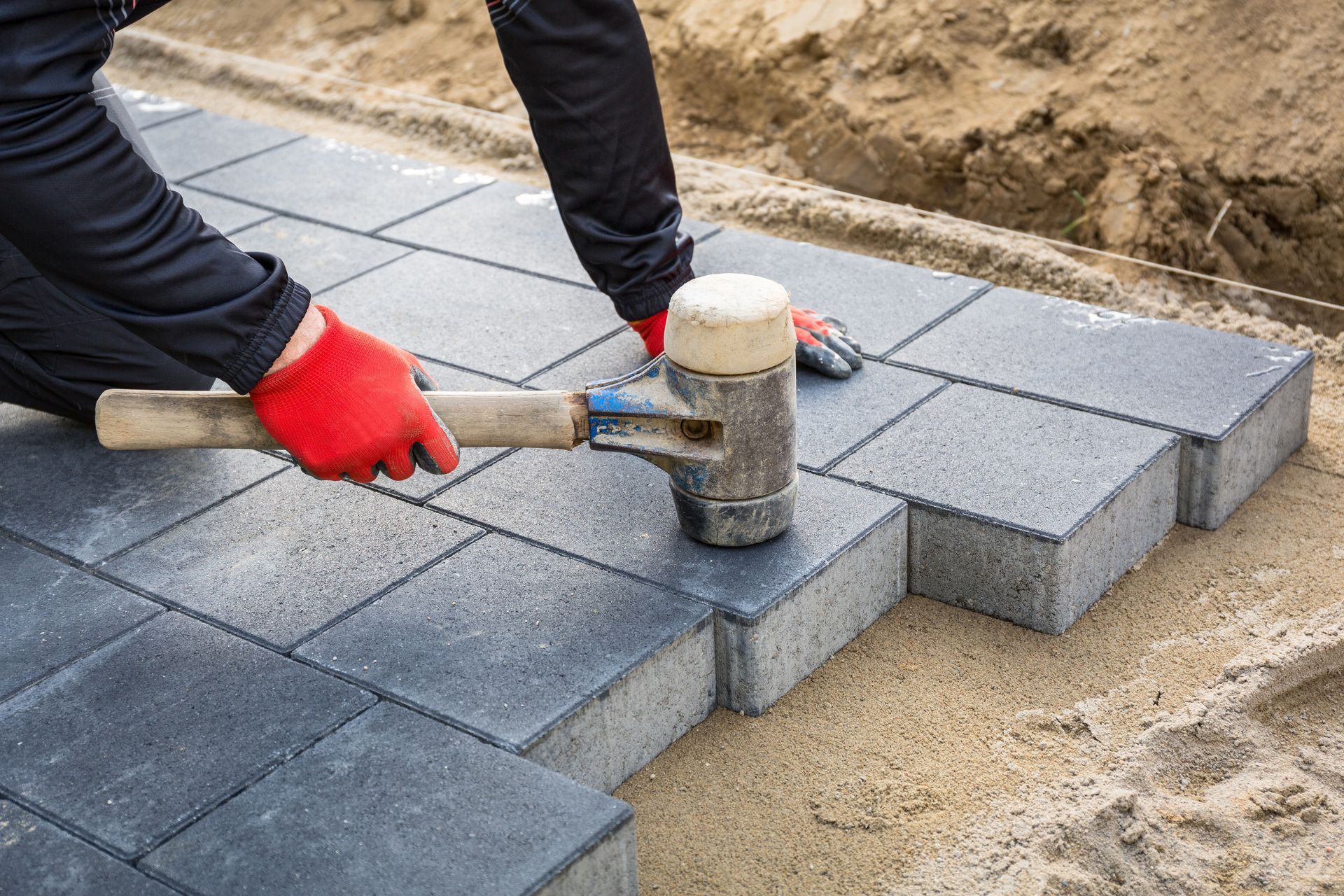 A man is using a rubber mallet to hammer bricks on a sidewalk.